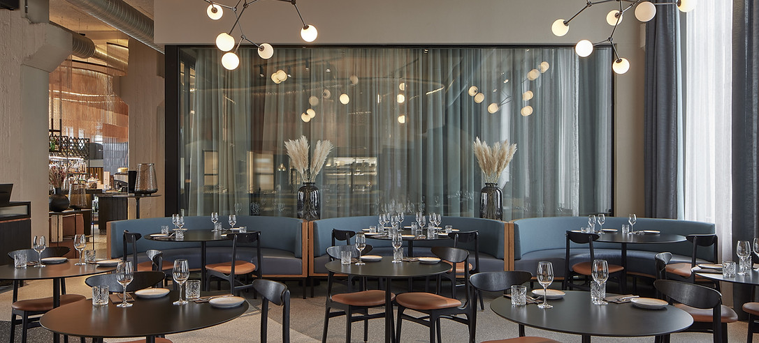 Modern restaurant interior with round tables, blue sofas, and elegant lighting.