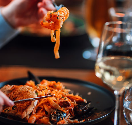 Manneskja með gaffal að borða sjávarréttapasta með hvítvínsglas til hliðar