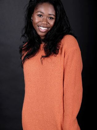 Young Black actress, Jamilah Rosemond, smiling in a bright orange sweater