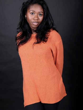 Young Black actress, Jamilah Rosemond, posing in a bright orange sweater