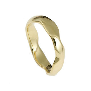 A close-up studio shot showcases a polished yellow gold ring against a stark white background. The ring has a smooth, flowing, and slightly irregular form, appearing almost fluid in its shape rather than a traditional band. The gold reflects light, creating highlights and curves that emphasize its three-dimensional nature. The ring casts a soft shadow directly beneath it on the white surface.