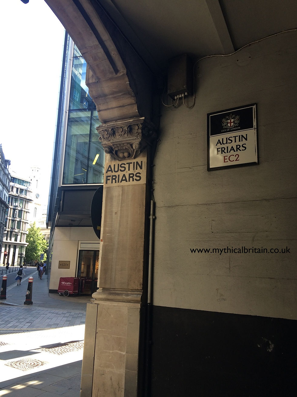 Entrance to an alleyway off a city street showing signs to the alley and city buildings in the background.