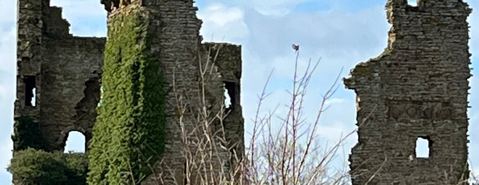 low wall in the foreground reveals the old castle behind with remains of a gatehouse and large tower