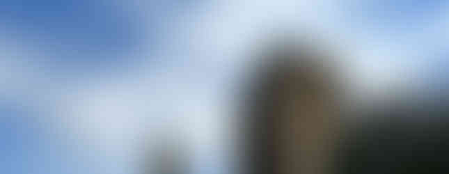 View from below showing trees and a mound with two huge towers on top against a blue sky
