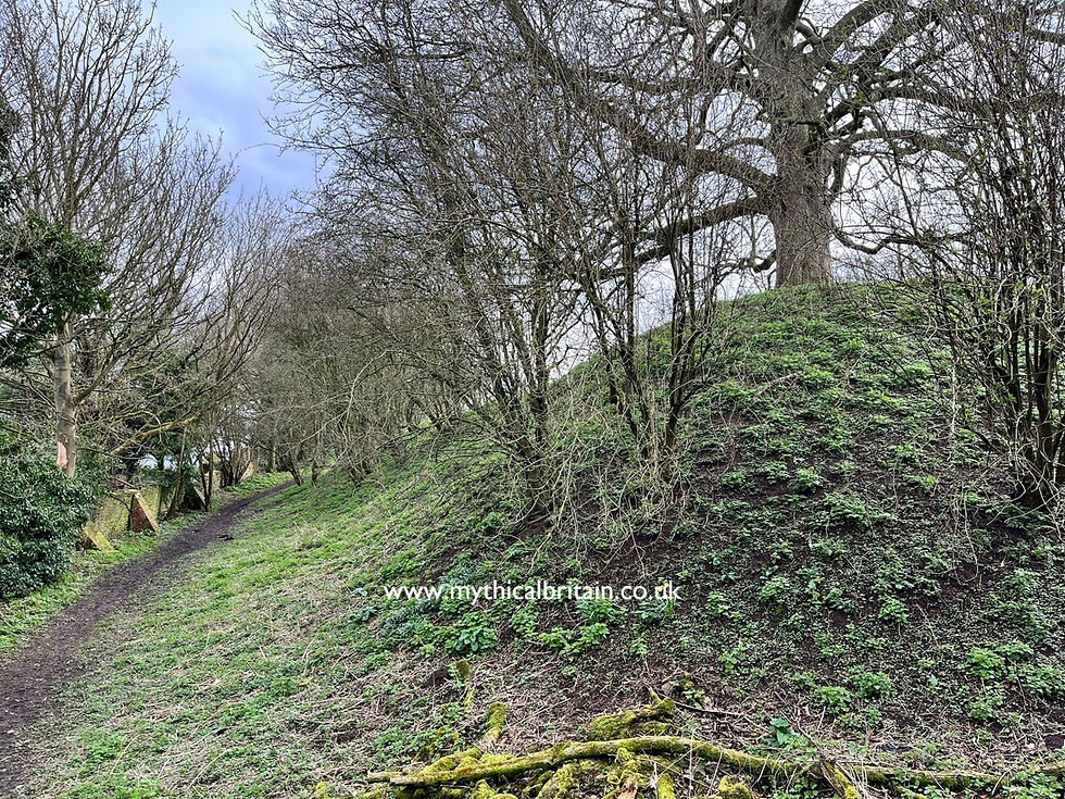 View showing a brick wall on the left dwarfed by an enormous earthen bank on the right with trees growing from it.