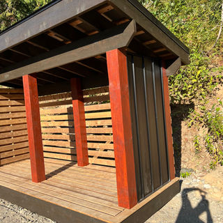 “Small timber-framed shed with stained posts, horizontal slat walls, and metal cladding panels.”