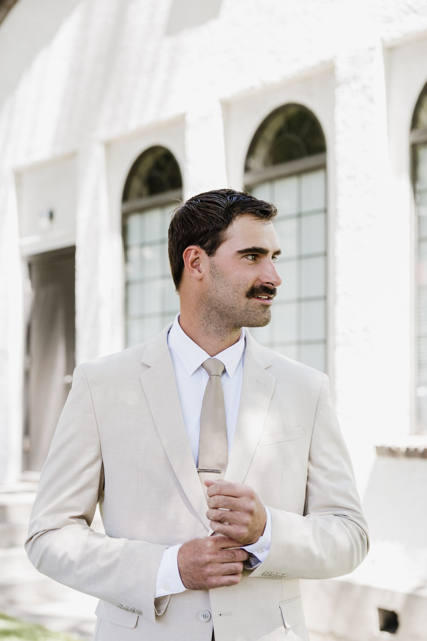A groom adjusting his cream suit outside a white building