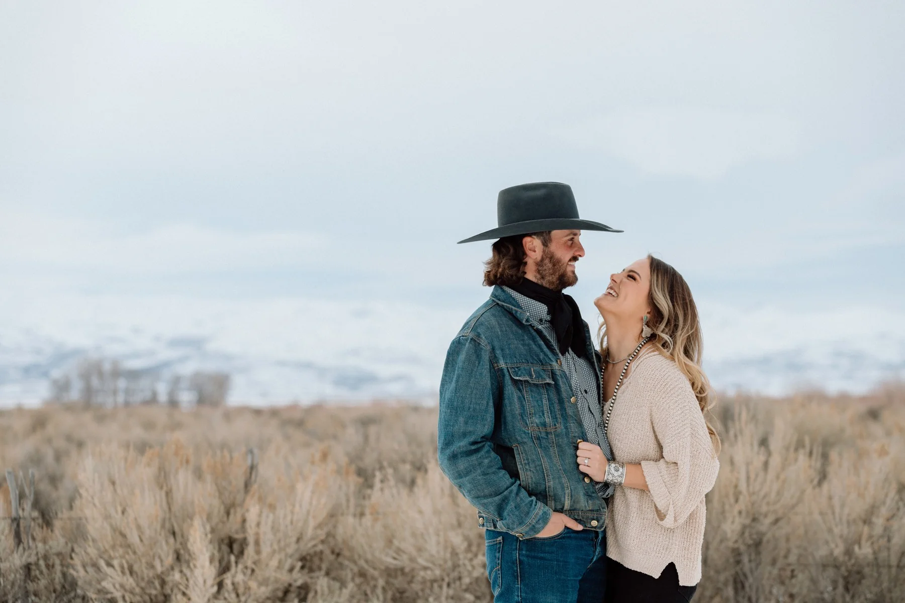 A couple embracing in a snowy field, one wearing a black cowboy hat