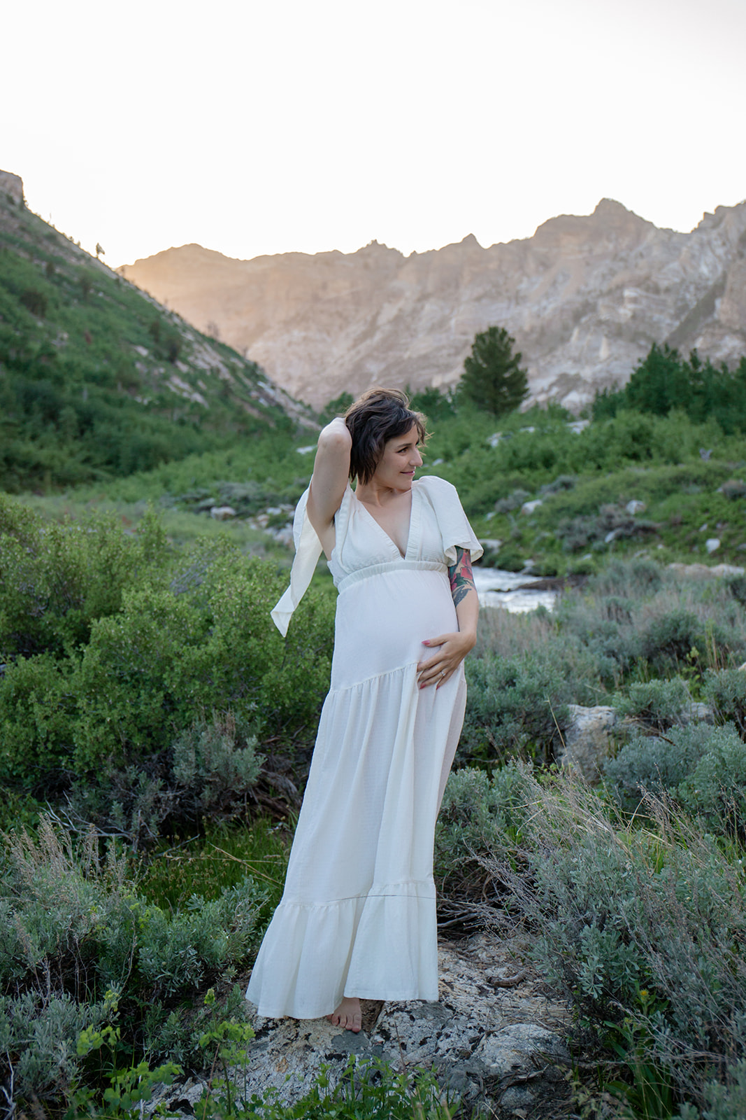 Emily in a white maternity dress beside a mountain stream