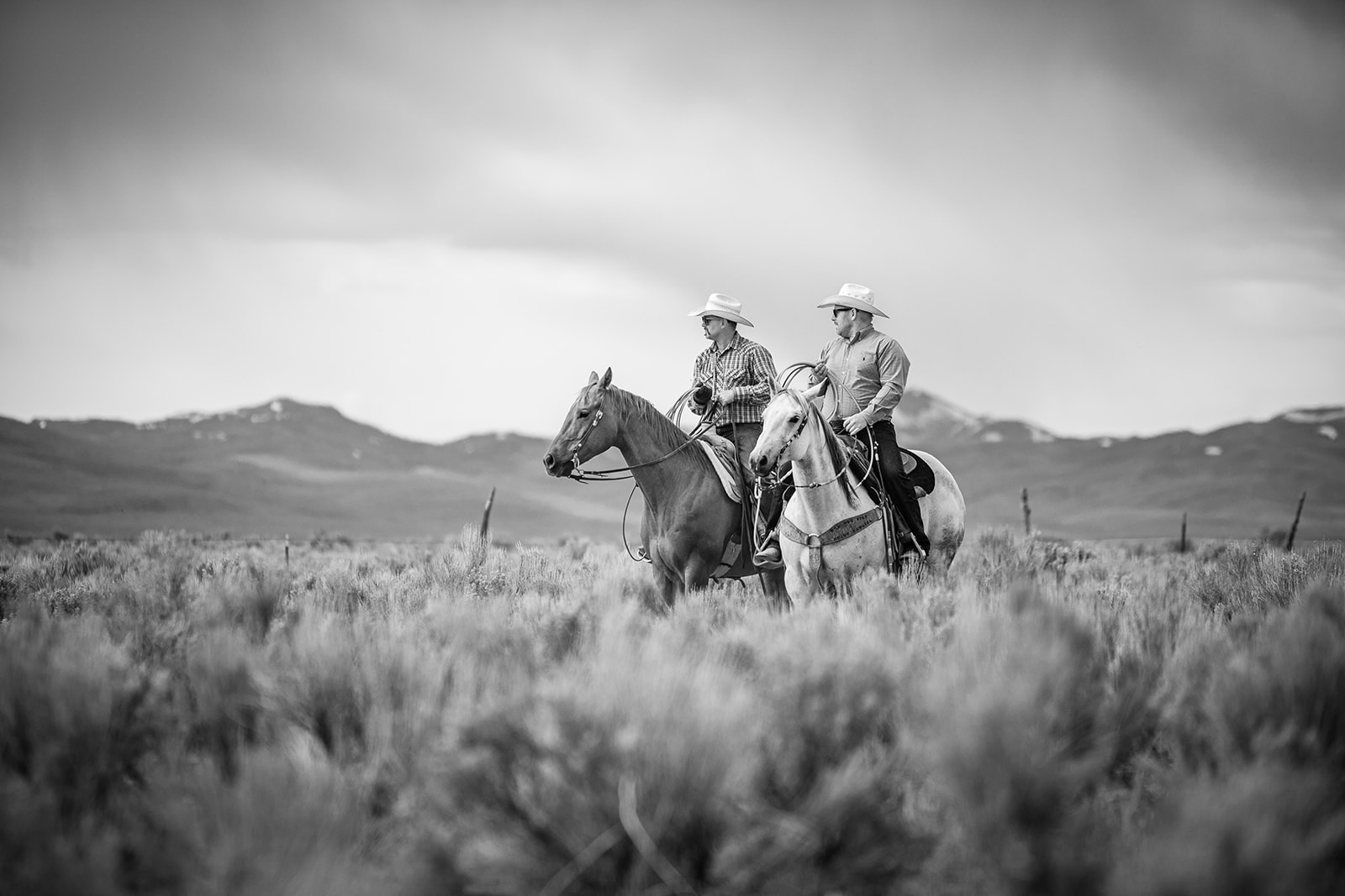 Two riders on horseback beneath the mountains, photographed in black and white