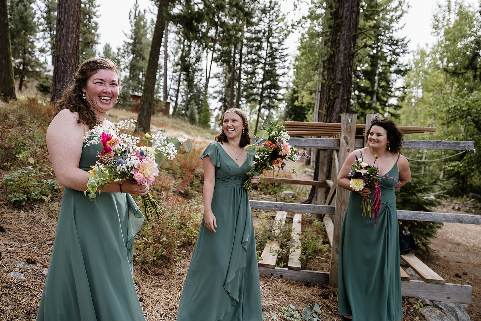 Emily and Sam’s bridesmaids laughing together with colorful bouquets beside a woodland fence