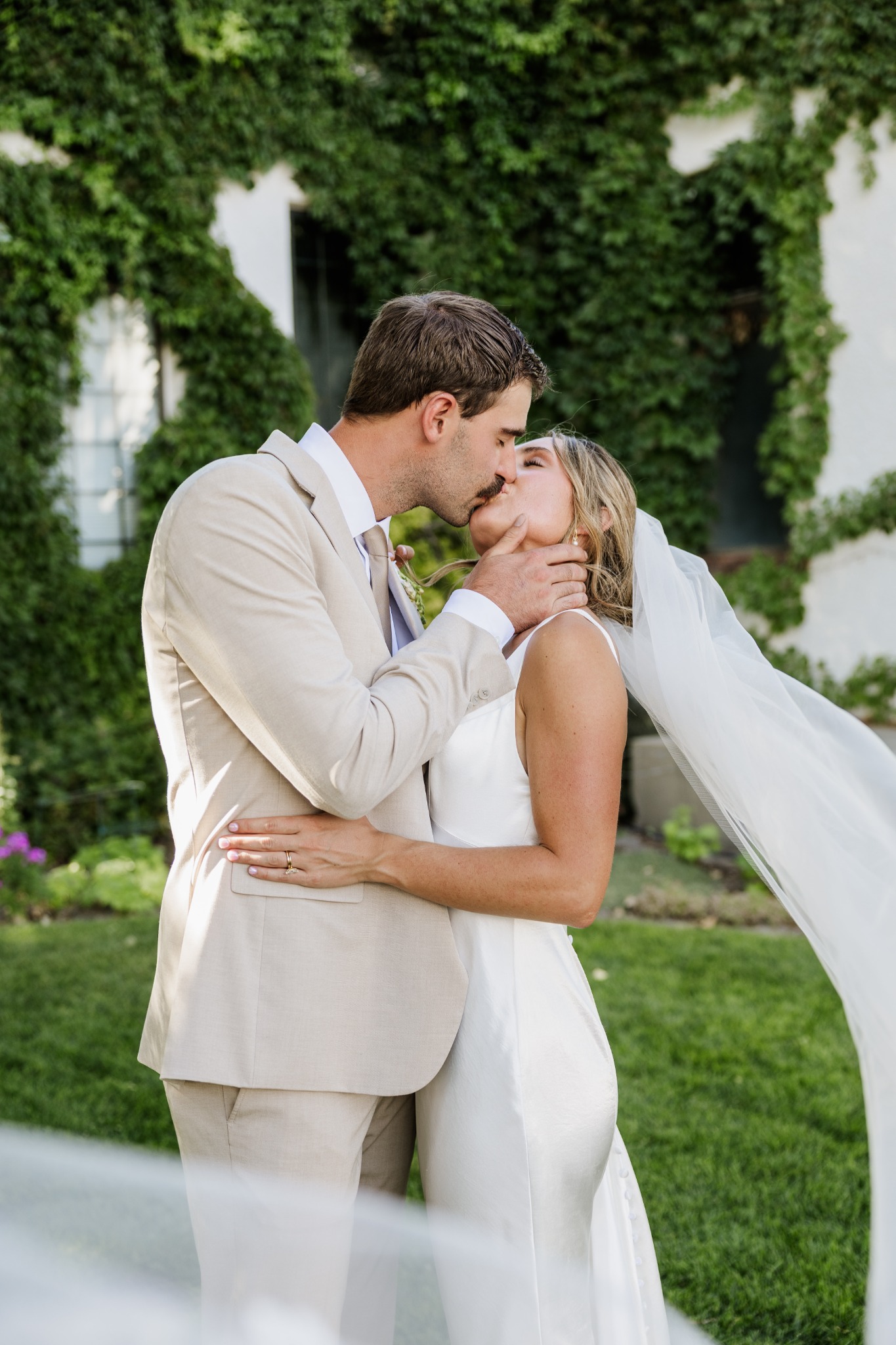 A newly married couple kissing beside an ivy-covered building