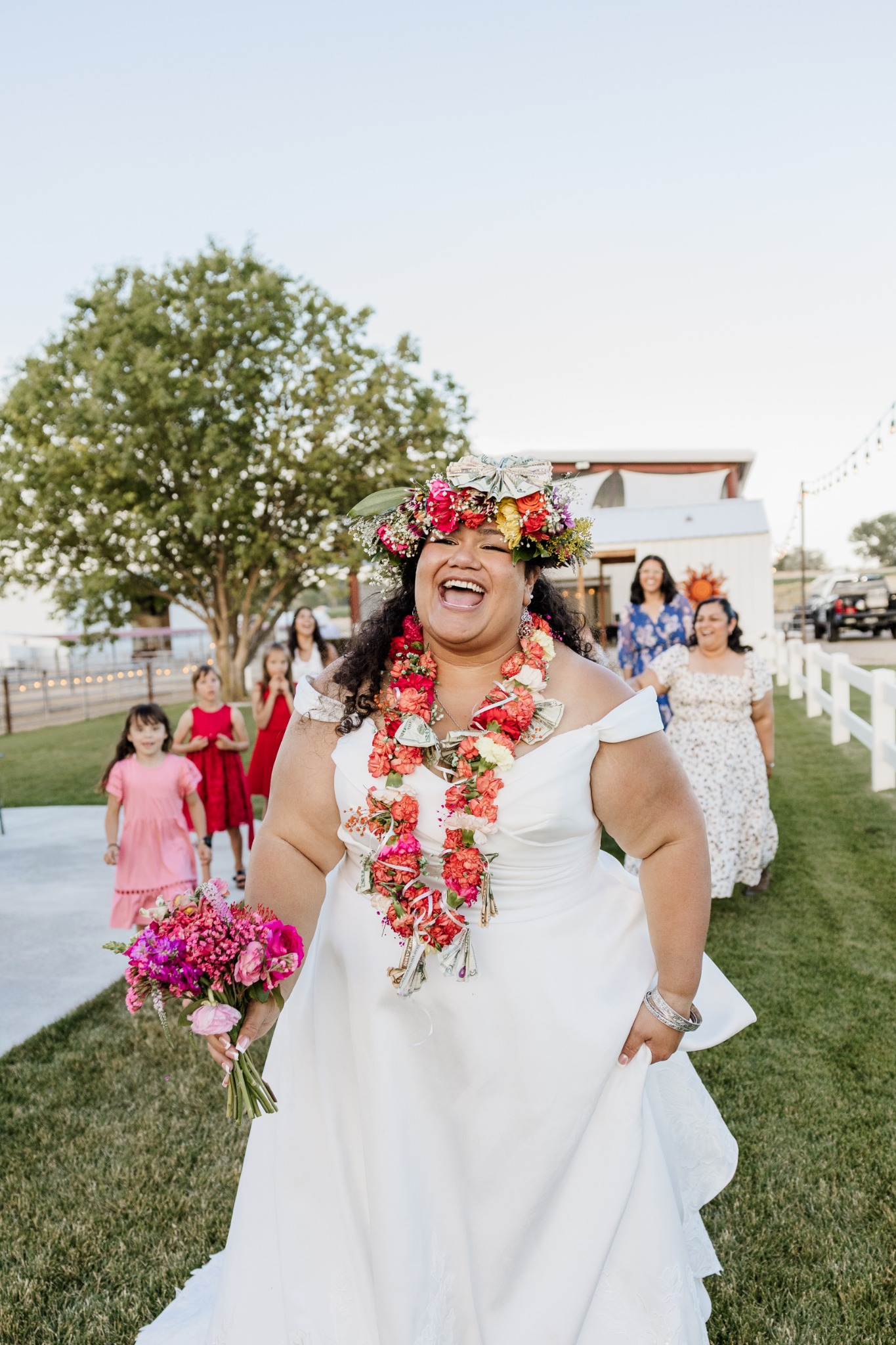 A bride laughing during an outdoor wedding procession, wearing a colorful floral lei