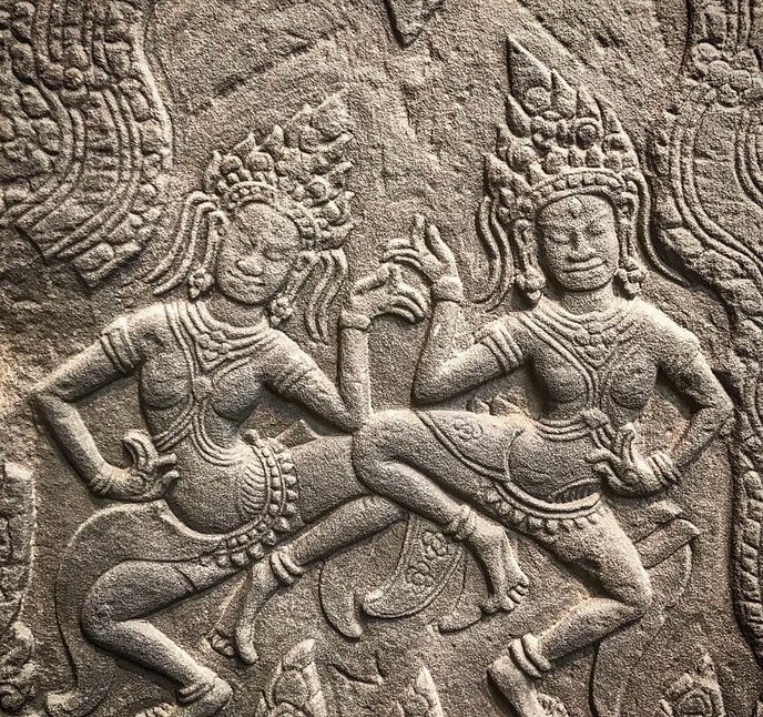 Stone carving of two dancing Angkorian figures wearing ornate headdresses and facing each other.