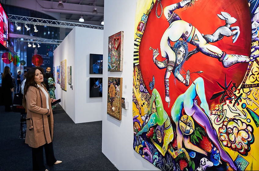 A visitor views a large, vividly colored Moschburg painting installed on a white exhibition wall.