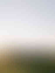 Bride and groom walking across a sunlit meadow at sunset during a fall wedding with rolling hills in the background