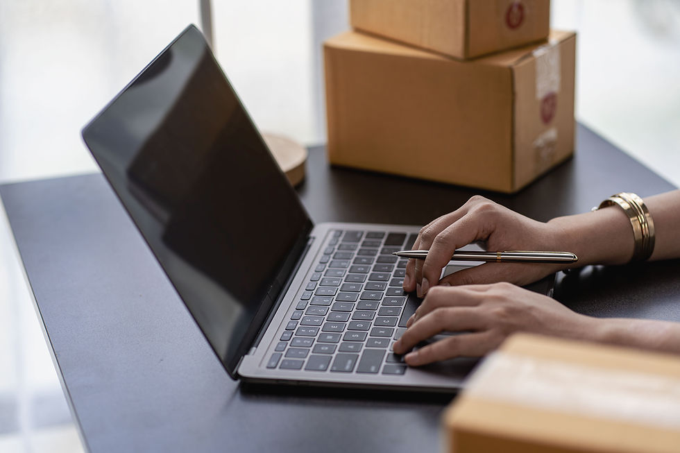 Person typing on a laptop at a desk with cardboard shipping boxes in the background