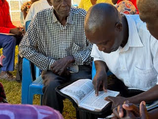 Men reading and discussing scripture together seated on blue chairs at outdoor EmPowered Living community gathering