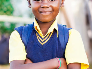 A young girl named Amina wearing her school uniform, standing confidently in front of Word Academy in Uganda.