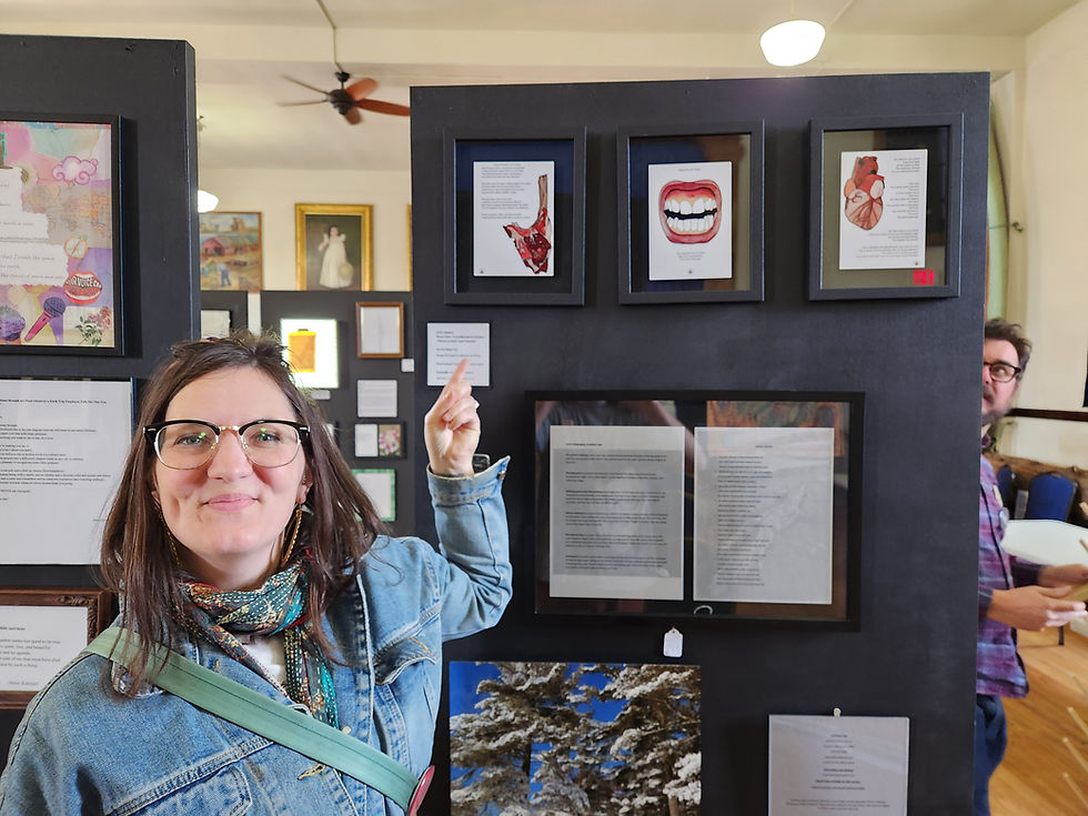 Me standing in front of my three framed pieces of art and watercolor at Frame It! Standing inside the Douglas County Historical Society with various colorful artworks on display.
