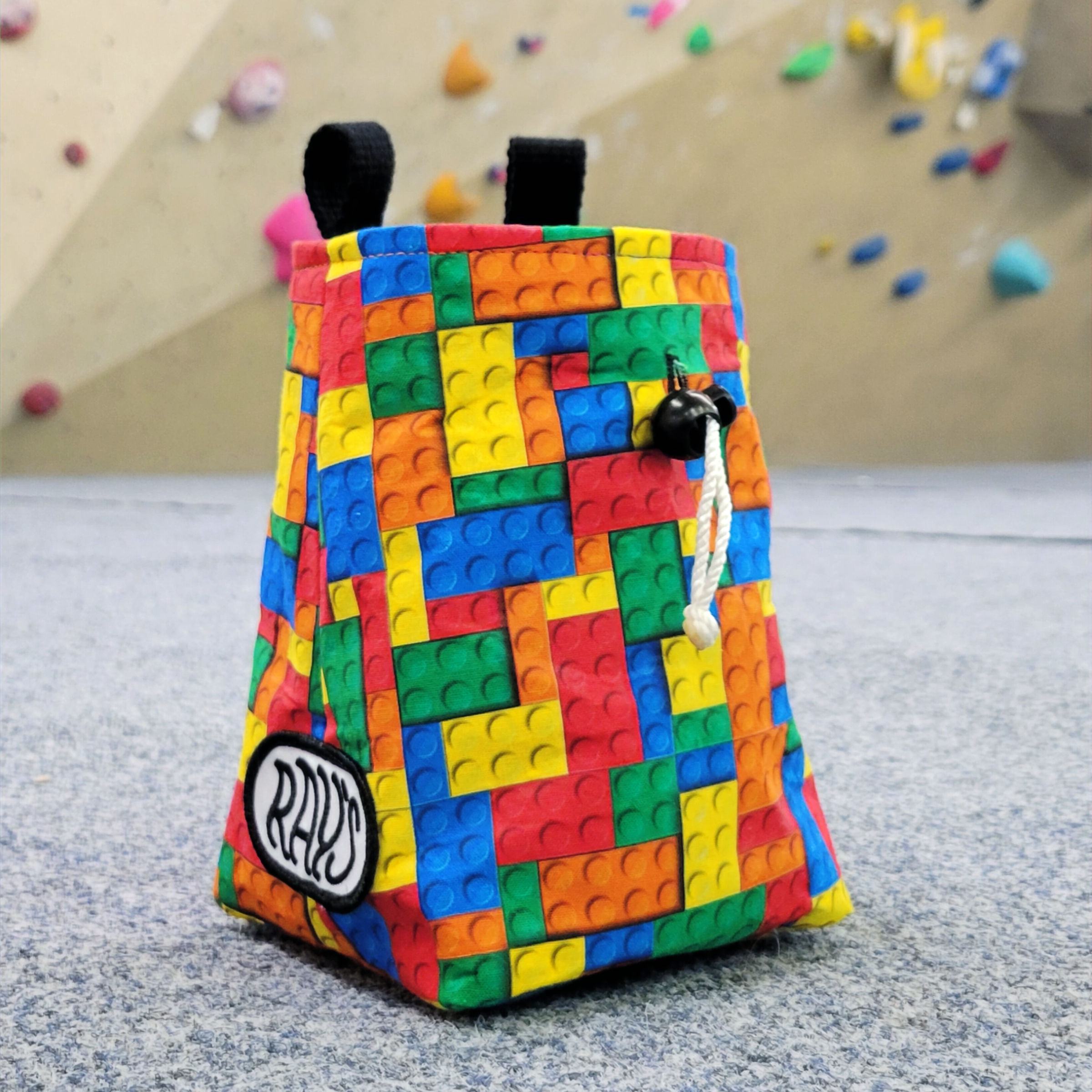 chalk bag made from a lego block patterned fabric, sat in front of a climbing wall