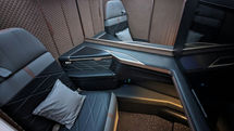 Luxurious airline seat with quilted walls and dark upholstery, featuring a plush pillow and sleek design. Mood is comfortable and sophisticated.