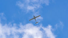 Diamond Da40 flying against a bright blue sky with scattered clouds, viewed from below. The scene feels serene and open.