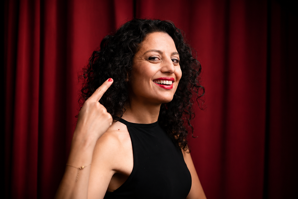 Başak Evran smiling with curly hair pointing to her head.