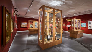 museum gallery with numerous custom wooden-glass display cases  and art on the walls