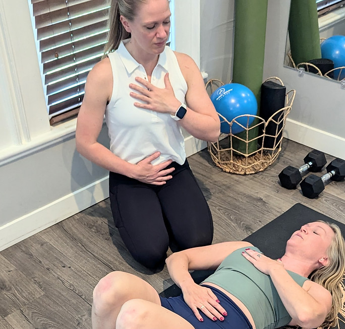 Physical therapist kneeling near patient with her lying on her back with her knees bent teaching breath work