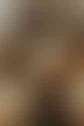 A woman in white leans on a man in a dark suit, seated in a rustic setting with flowers and a wooden table. Vintage, romantic mood.