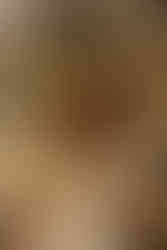 A woman in white leans on a man in a dark suit, seated in a rustic setting with flowers and a wooden table. Vintage, romantic mood.