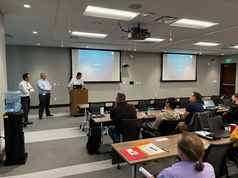 Speaker at podium presenting to people in a modern conference room.
