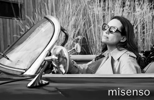 Black and white Misenso sunglasses campaign — woman wearing oversized cat-eye frames in a vintage convertible car, photographed by Simon Clemenger