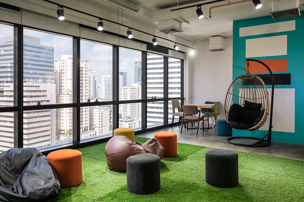 Ambiente corporativo com grama e puffs para descanso,