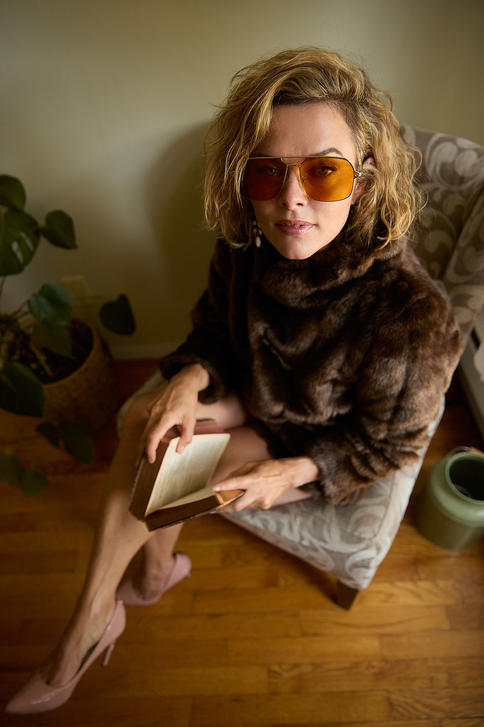 Actor Erin Boyes sits in a chair wearing a fir coat and reading a book