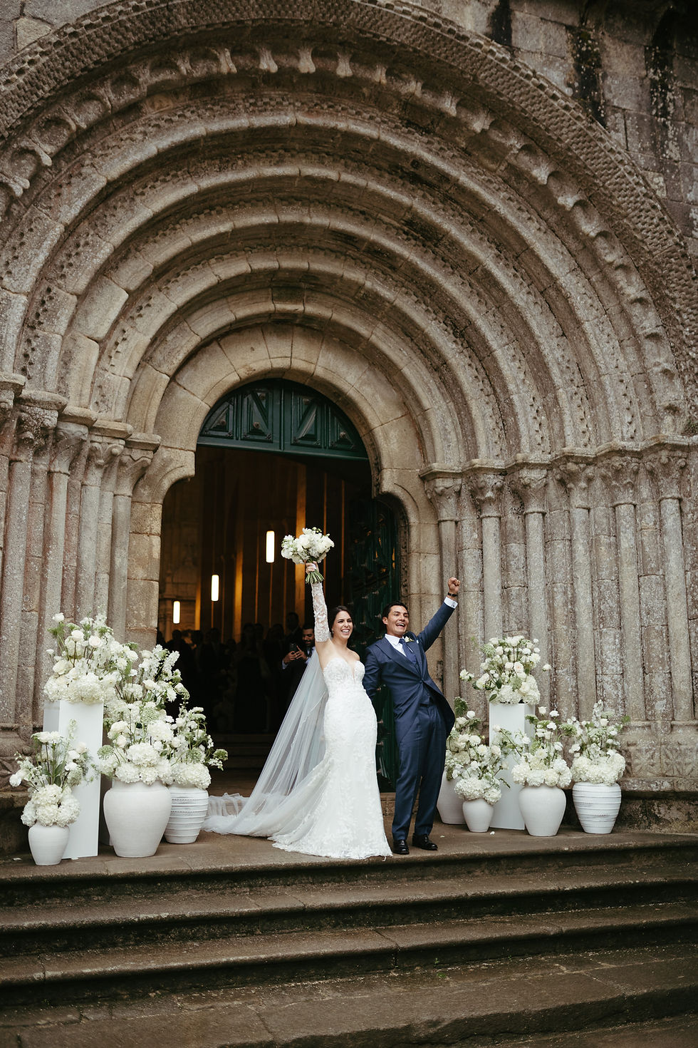 Belén y Adrián en la entrada del Monasterio de Armenteira, rodeados de la decoración floral de su boda de destino en Galicia