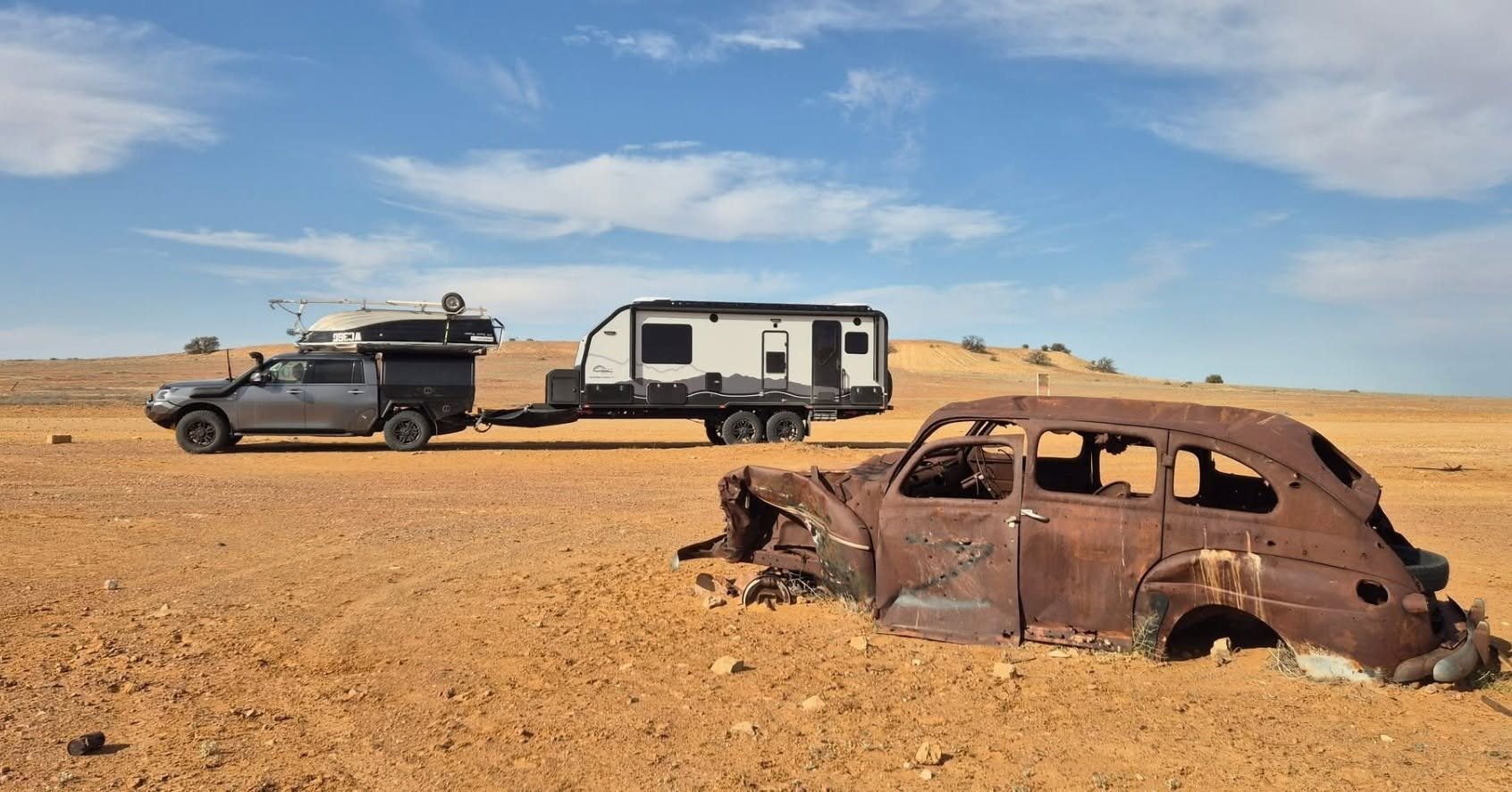 An Offroad Grit RV and ute in red desert country, past an old rusted car
