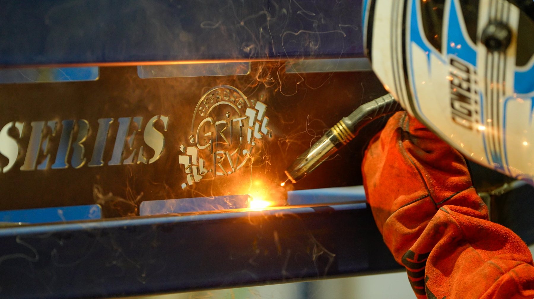 Welding the Offroad Grit RV name into a chassis rail, in full helmet and welding gloves