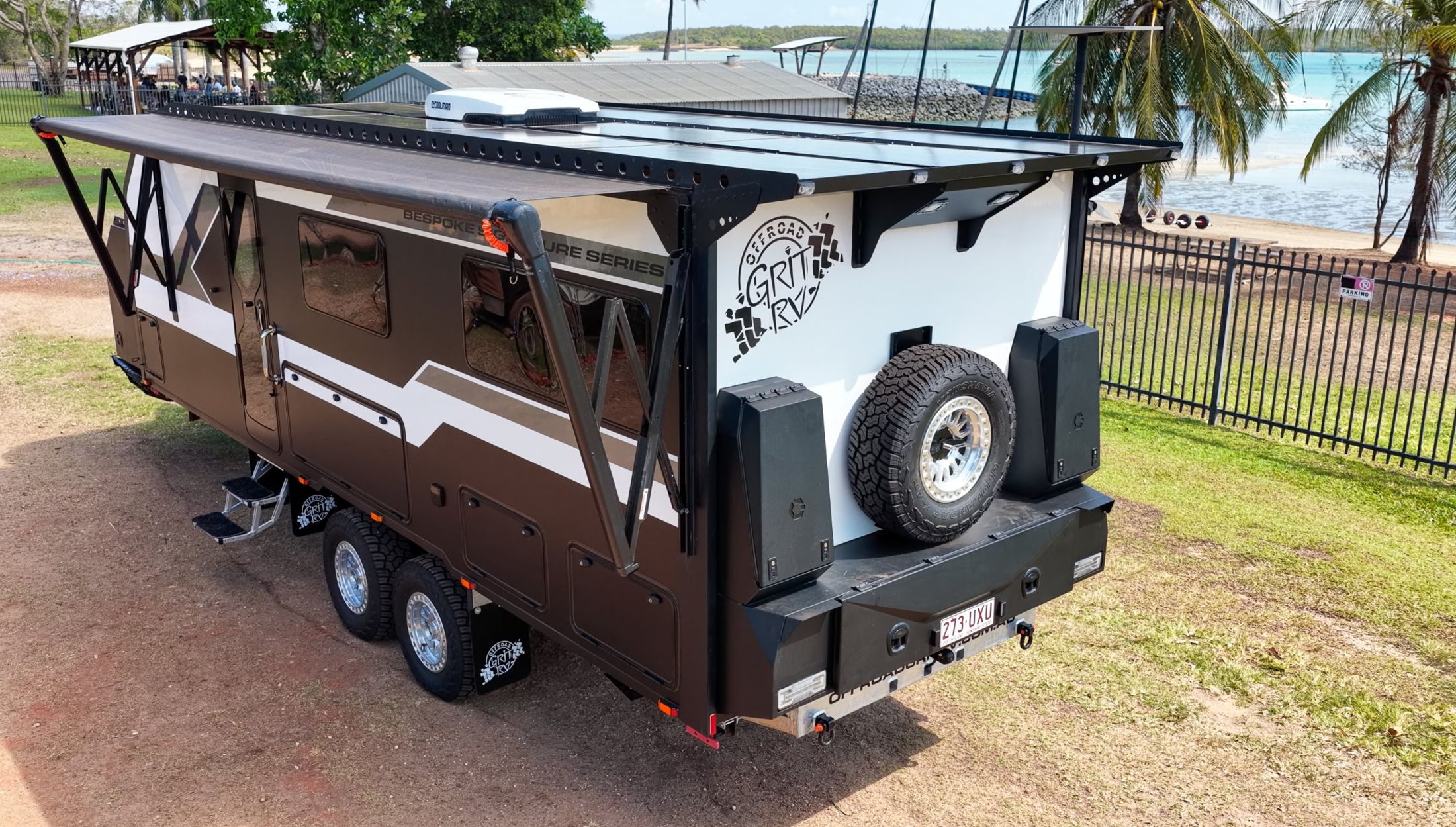 Rear quarter of an Offroad Grit RV composite caravan with spare wheel and storage boxes, beside the water