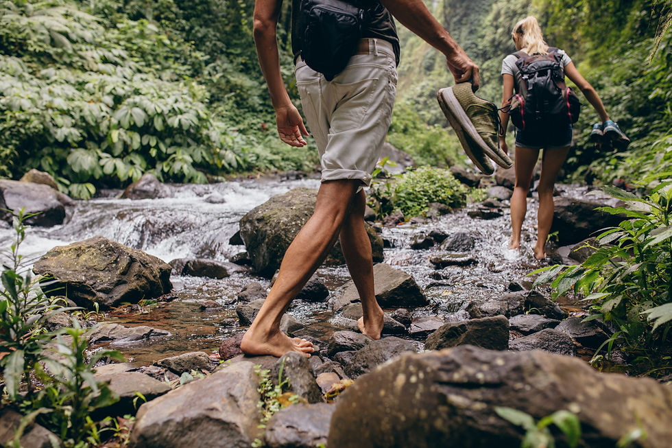 Couple walking barefoot through rocky jungle stream.