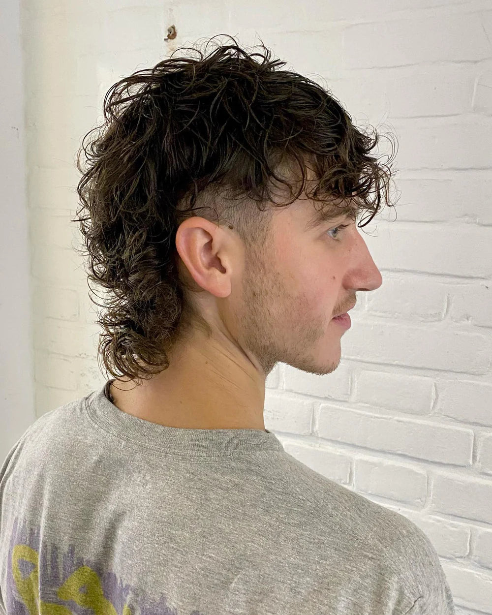 Man posing looking to the right in front of a white brick wall