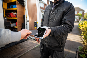 A customer paying a UK tradesperson via a contactless card reader displaying an approved payment outside a work van.