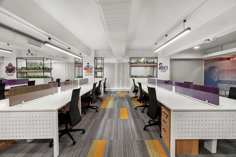 Modern office interiors with long shared desks, purple dividers, and greenery accents – vibrant workspace design in Bengaluru