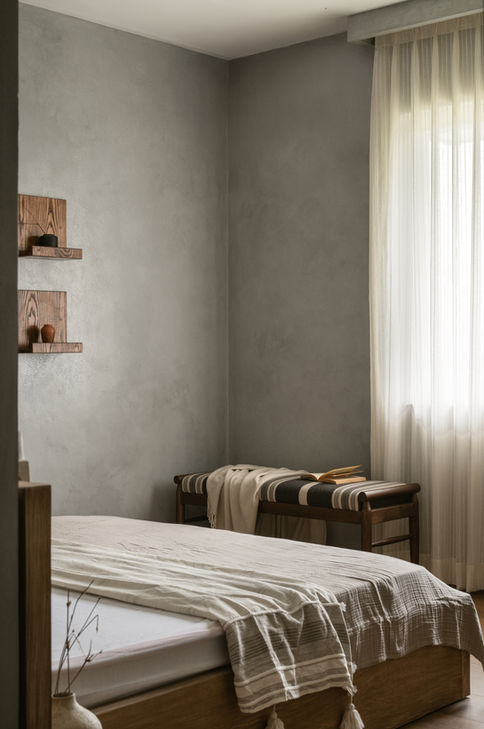 Minimal guest bedroom with lime-plaster walls, wood bed, and striped bench – modern Wabi Sabi interior