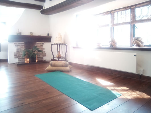 YASMINA'S Yoga space, cushions sitting on blue yoga mat on a wooden floor with fireplace in the background