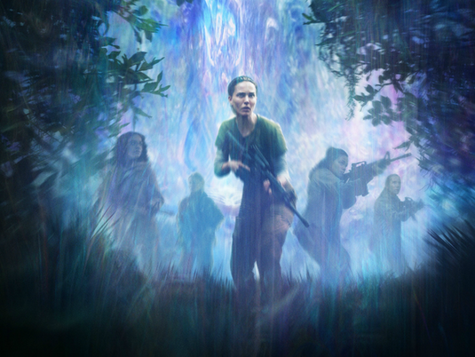Annihilation poster image featuring the star of the movie holding a machine gun, walking through an environment of prismatic light and plants.
