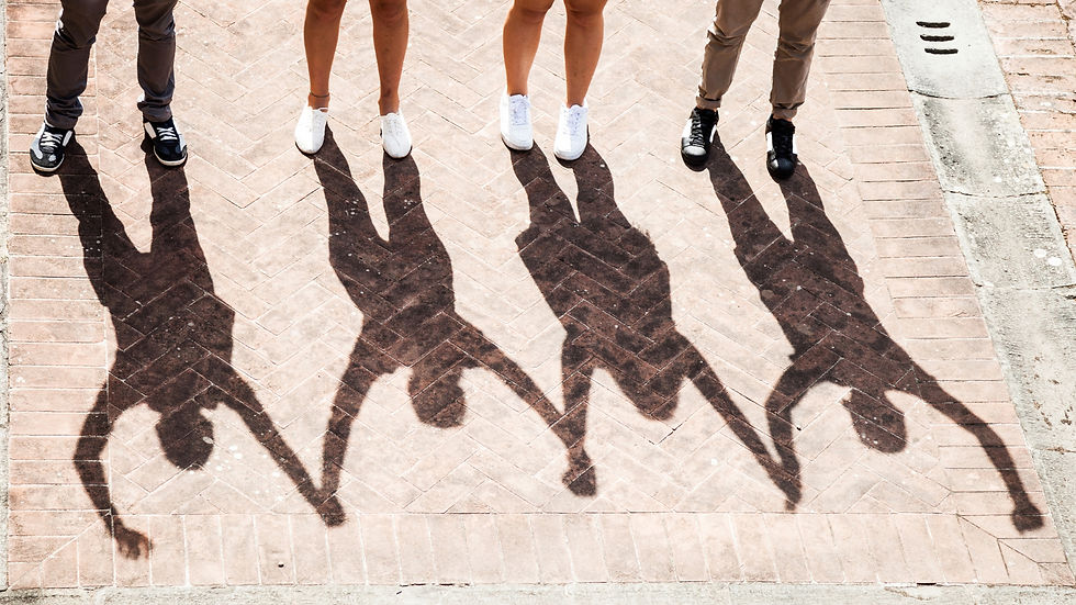 Shadows of four people holding hands on a sunlit brick pavement. Only their feet and lower legs are visible, suggesting a sense of unity.