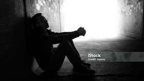 Silhouetted man sits curled up in a concrete tunnel, facing bright light; iStock Credit: baona and 2149642583 visible.