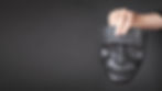 A hand holding a black mask against a dark background, representing the act of hiding one's true identity and the emotional burden of pretending.